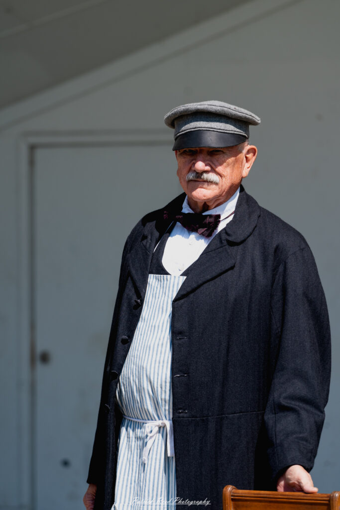 A man dressed in Civil War period clothing, standing confidently while posing for the camera. His outfit includes a frock coat, waistcoat, and period-appropriate trousers, reflecting the fashion of the era. The scene captures his character and the historical significance of the time.